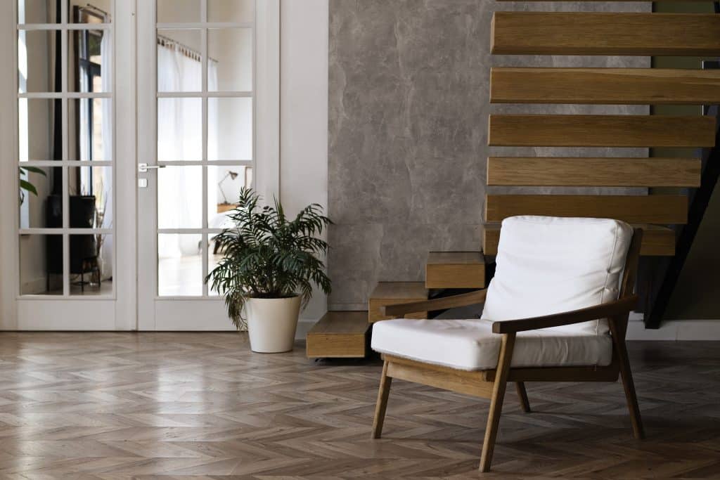 Aménagement d'un salon lumineux avec fauteuil blanc et escalier en bois, illustrant l'harmonie des volumes en architecture d'intérieur.